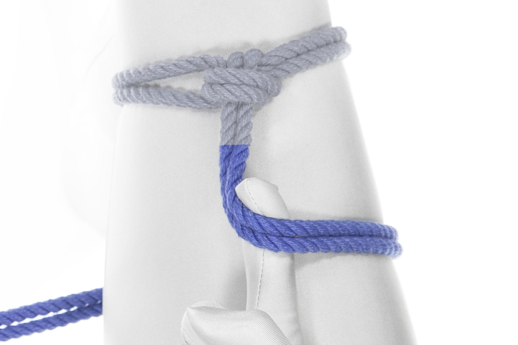 A blue rope has been tied around a thigh in a single column tie with a single wrap. The rope comes toward the body for three inches, then turns to the right and goes clockwise around the thigh. The rigger’s right index finger hooks under the rope at the turn, keeping it at 90 degrees.
