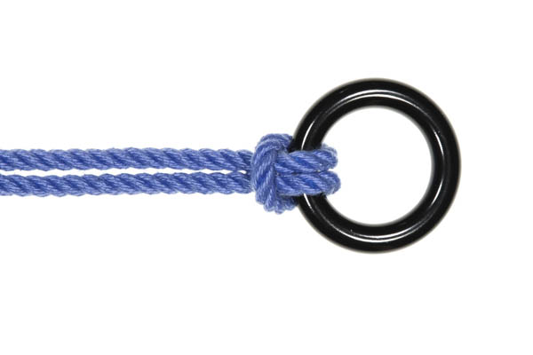 A doubled blue rope is attached to a shiny black rappel ring with a lark’s head. The rope enters from the left of the frame and crosses over the left side of the ring. It the crosses back under the ring and the bight of the rope goes over the standing part.