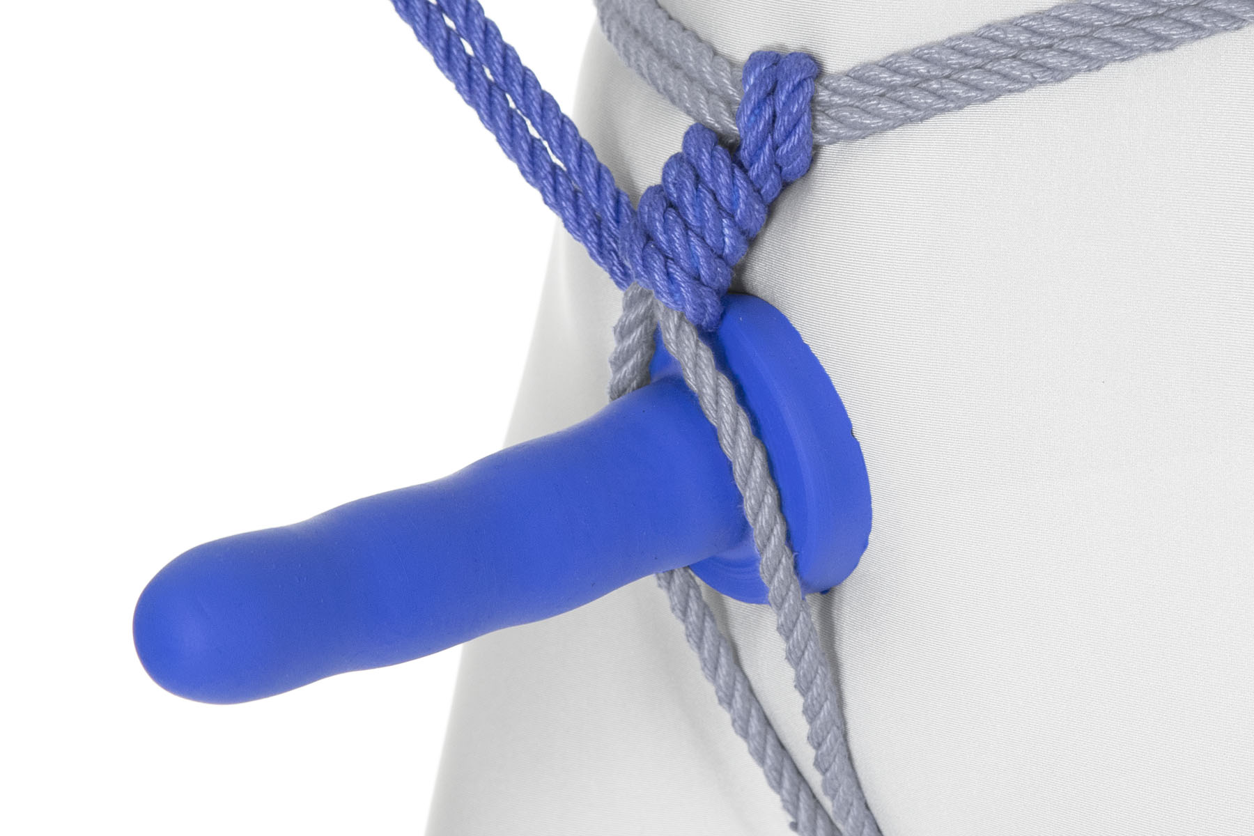 The rope comes back over the waist line and makes three tight spirals around itself, moving down. A blue dildo has been inserted between the two strands of the rope and pulled up snug against the spirals. The base of the dildo is against the pubic mound and it sticks straight out.