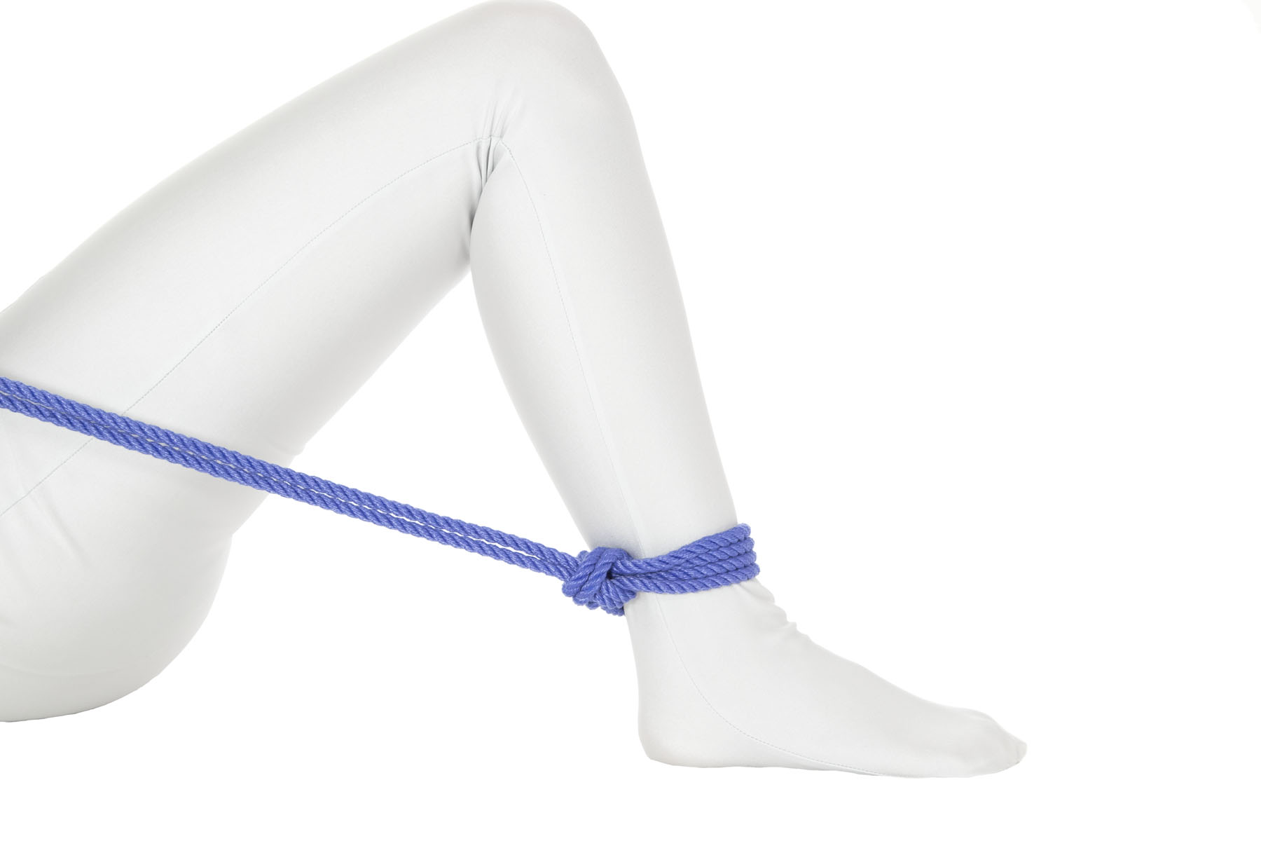 A person in a white bodysuit is lying on their back. Their right leg is fully bent, with the foot flat on the ground and the knee pointing upward. A single column tie has been tied around the right ankle and the rope crosses over the right thigh just below the hip.