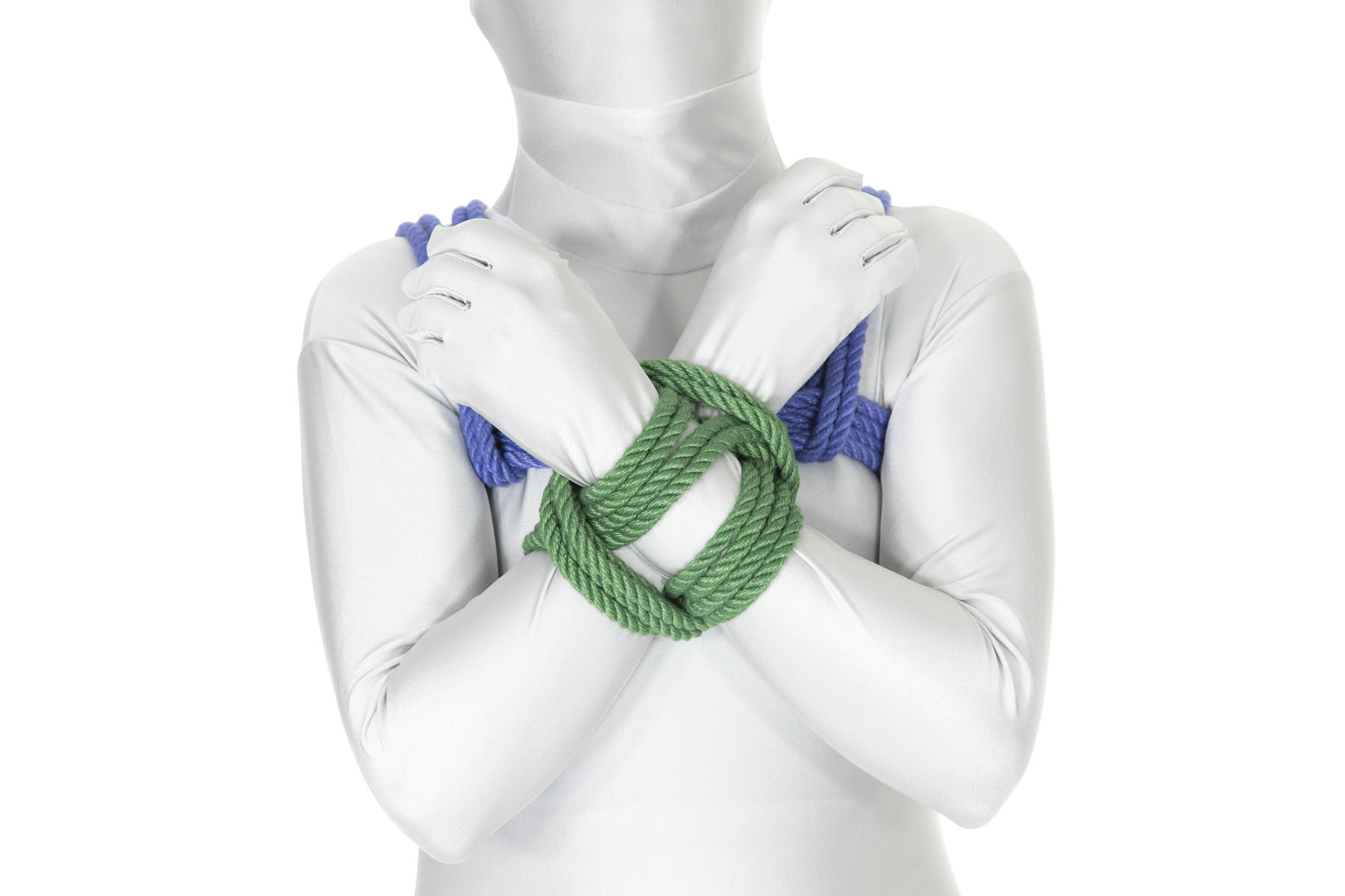 A person in a white bodysuit wearing a blue chest harness. Their arms are crossed at the wrists right over the breastbone. A square lashing in green rope binds their wrists together.