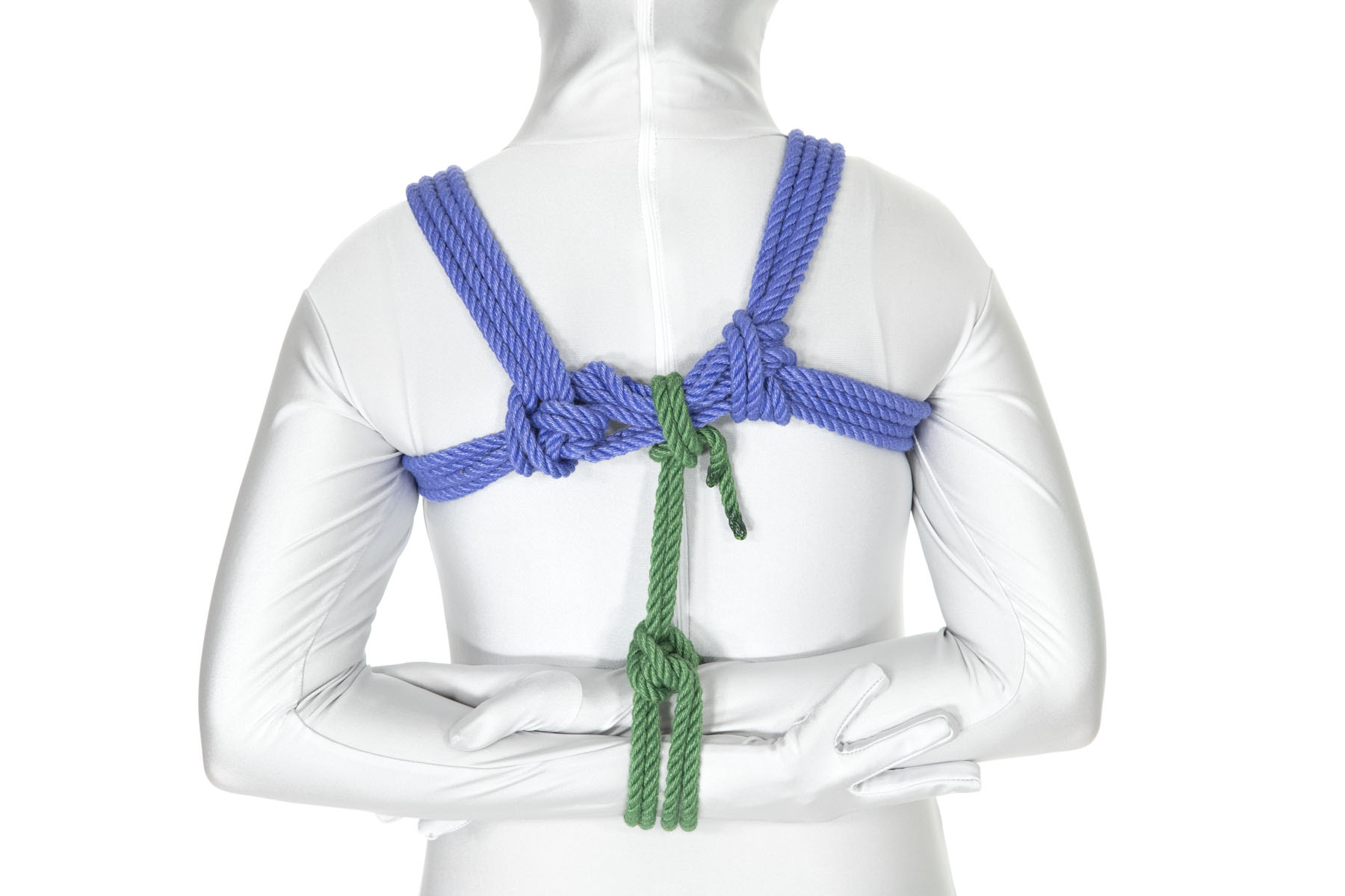 A rear view of a person in a white bodysuit wearing a blue chest harness. Their forearms are horizontal behind their back in an antiparallel position. The arms are bound together with a column tie in green rope and the tail of the green rope is tied off to the chest harness.