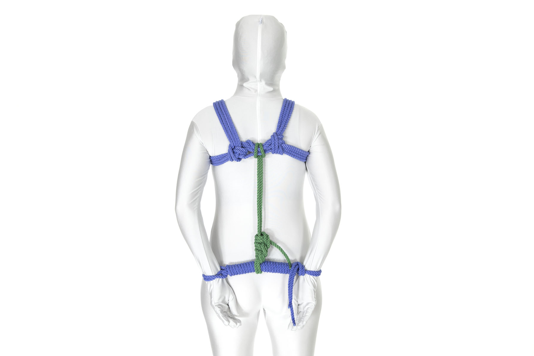 A rear view of a person in a white bodysuit wearing a blue chest harness. Their arms hang straight down, slightly behind their back, with the backs of the hands resting on the buttocks. The wrists are separated by about eight inches and are bound together by a bar tie in blue rope. A green rope connects the center of the bar tie to the chest harness.