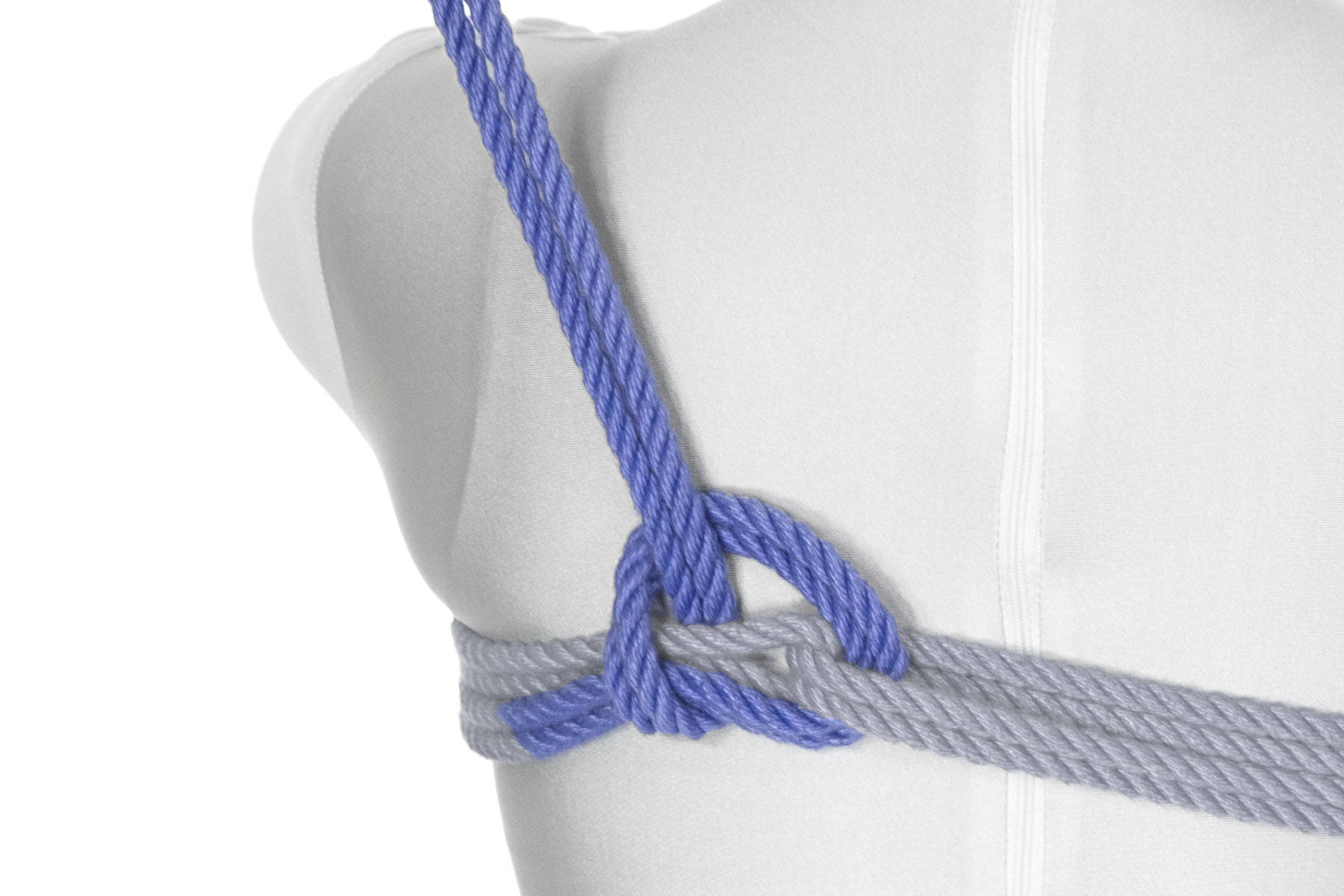 The rope goes over the chest wraps just to the left of the bight, back under them, and then over itself, making a half hitch. The end of the rope exits the half hitch in the direction of the left shoulder.