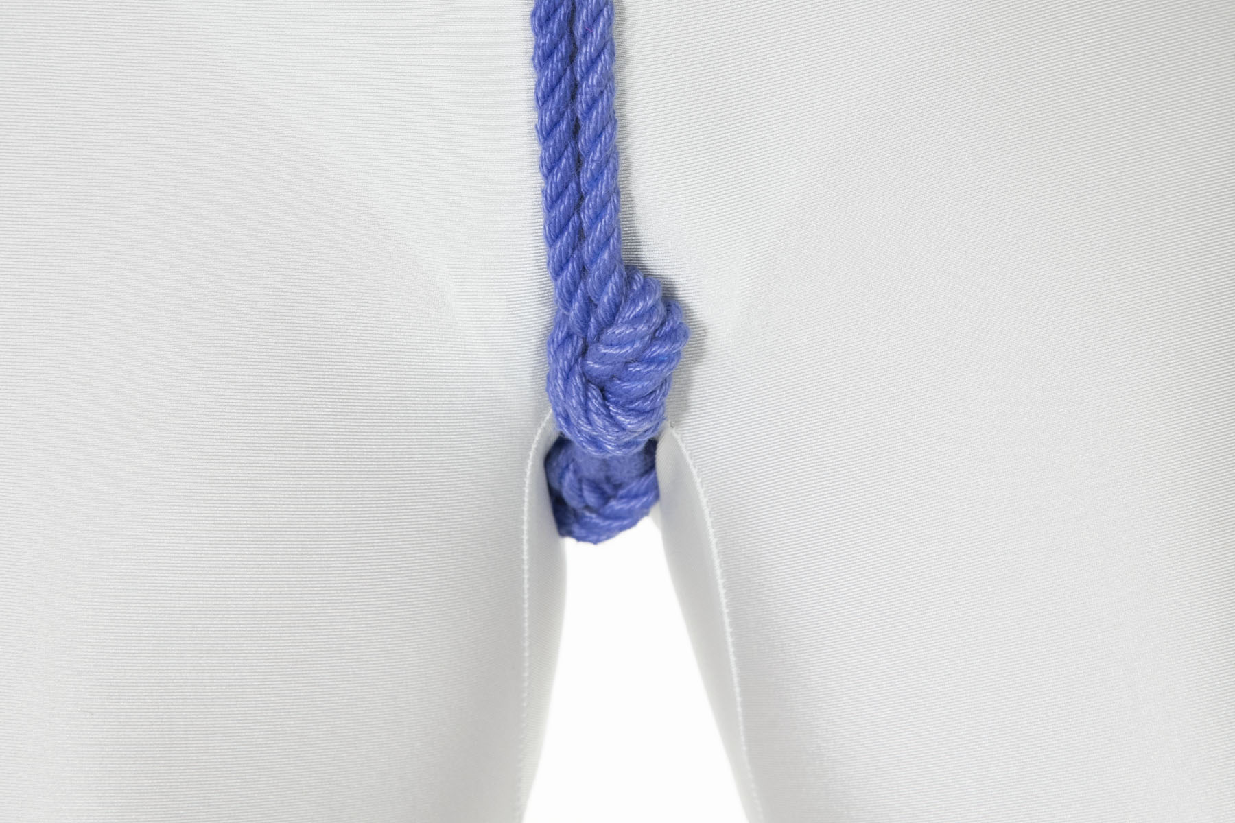 A closeup of the rope as it passes between the legs and goes over the crotch. Several overhand knots have been tied in the rope to create pressure points over the genitals.