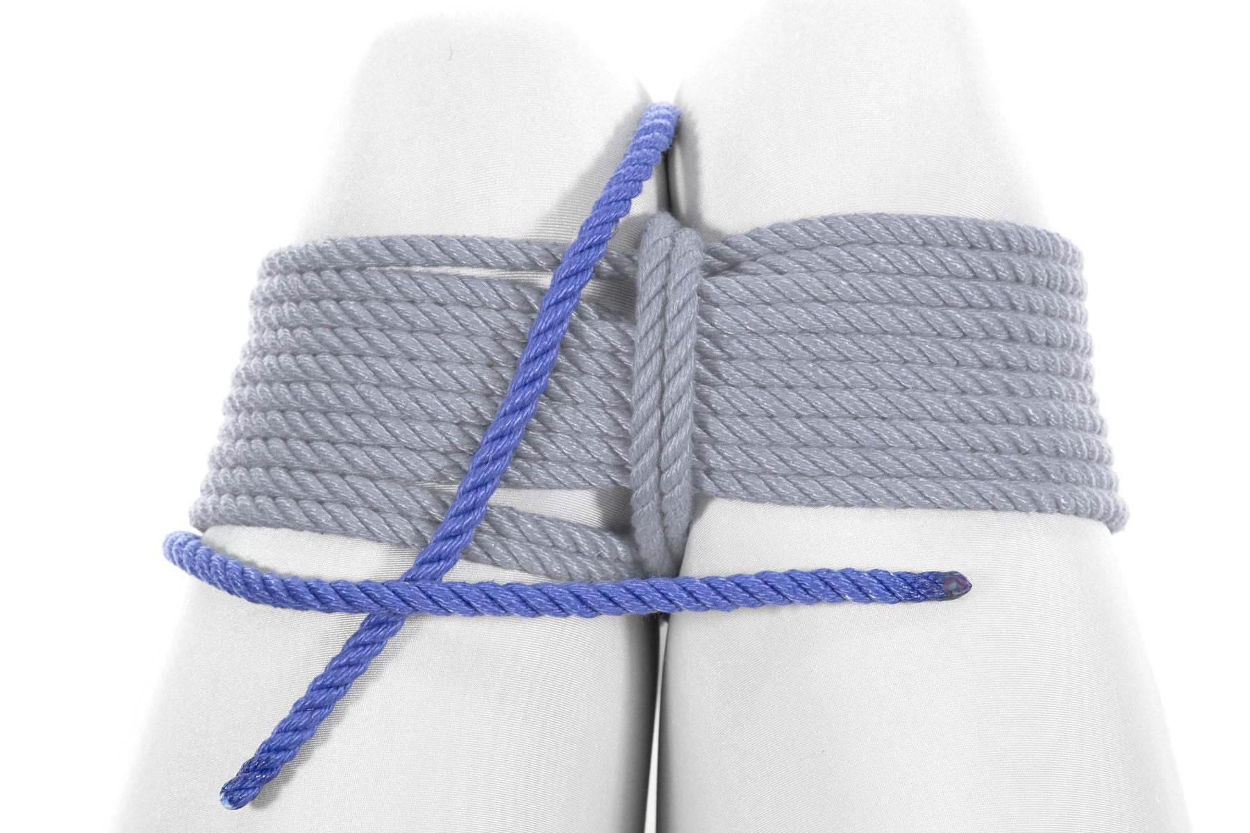 The two ends of the rope have been separated. One comes up between the knees, right where it did previously. The other end has gone clockwise around the left leg. The two ends cross each other on top of the left leg.