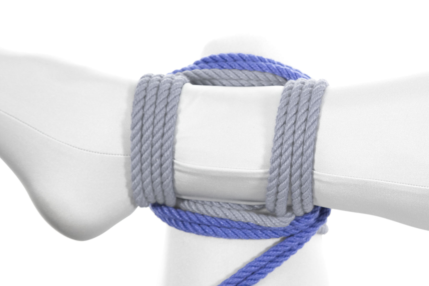 The rope now makes a second full square, crossing left over the left leg, moving away from the body under the right ankle, crossing right over the left leg just above the knee, and coming back toward the body under the right leg. It again ends up in the lower right of the frame.