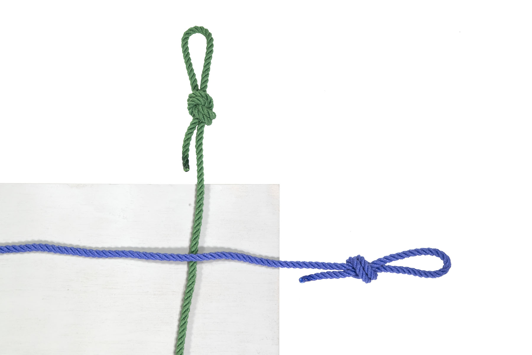 This is a closeup view of the top right corner of the board. A green rope crosses the board vertically, about three inches inside the right edge of the board and a blue rope crosses the board horizontally, about three inches below the top edge of the board. The ends of both ropes have been tied in overhand loop knots, making loops that are about three inches long.