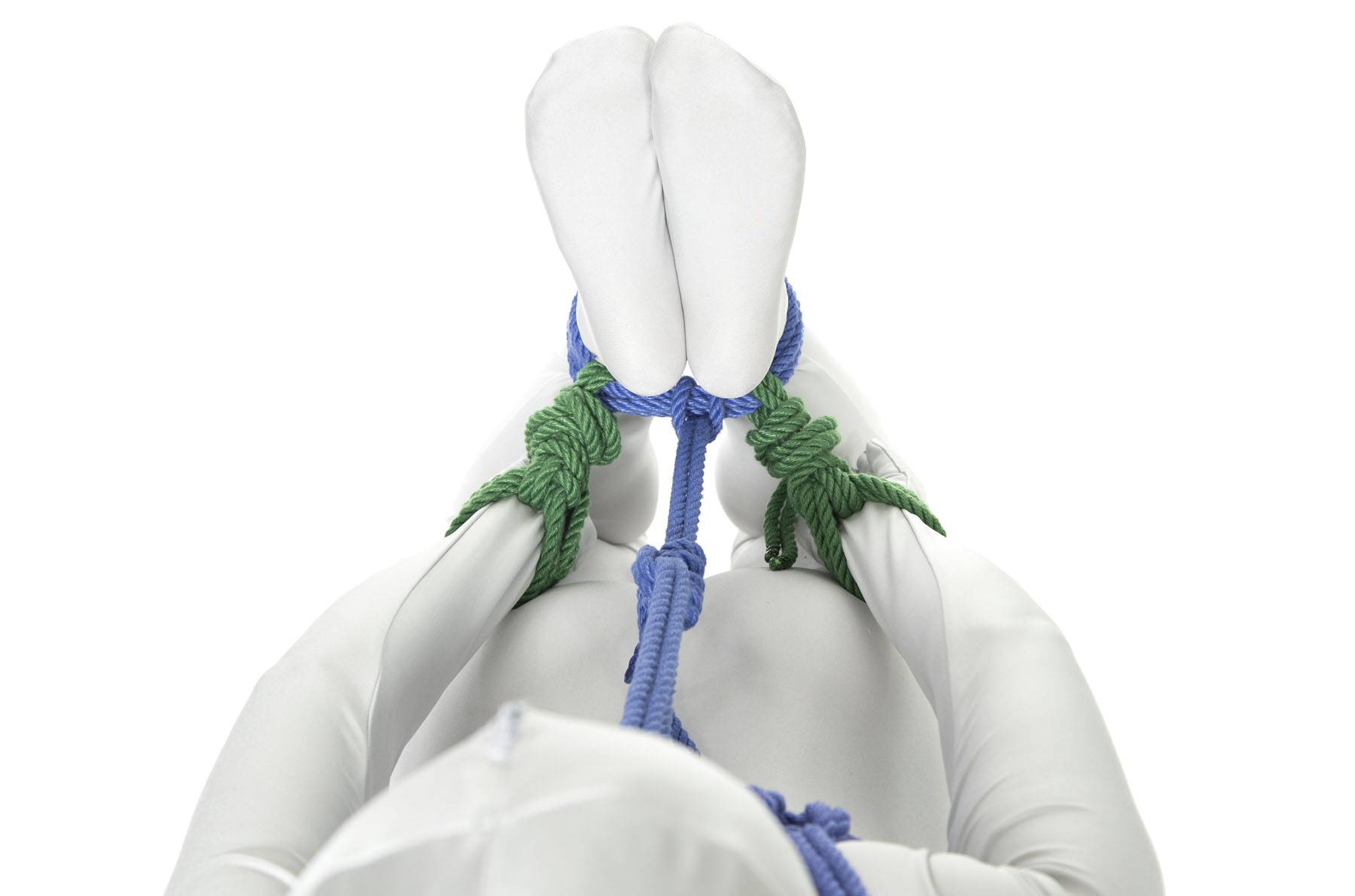 We are looking over the head of a person in a hogtie toward their feet. We can see a little bit of the chest harness and have a clear view of the line connecting the chest harness to the ankles. The wrists are not tied together and are parallel to the body, reaching back toward the ankles. Each wrist has a single column tie in green rope that is attached to the ankle on that side. The separation between the wrist and ankle ties is only a few inches.