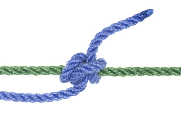 A green rope crosses the frame horizontally. A blue rope enters from the left of the frame and is tied to the green rope with a midshipman’s hitch. Two spirals of rope are wedged together on the left side of the knot and a half hitch is on the right. The knot is pulled tight and snug, but looks less tidy than an adjustable grip hitch.