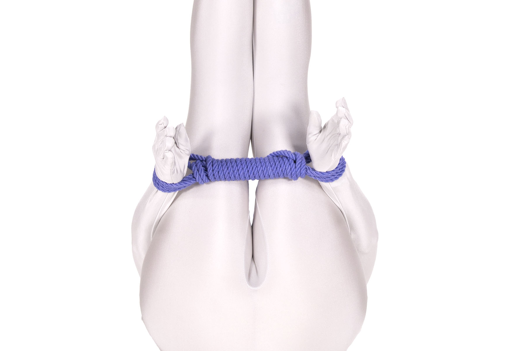 A person in a white bodysuit is lying on their back with their legs straight up in the air. Their hands are held next to their knees and their wrists are tied together with a long bar tie in blue rope. The bar tie passes right behind their knees.