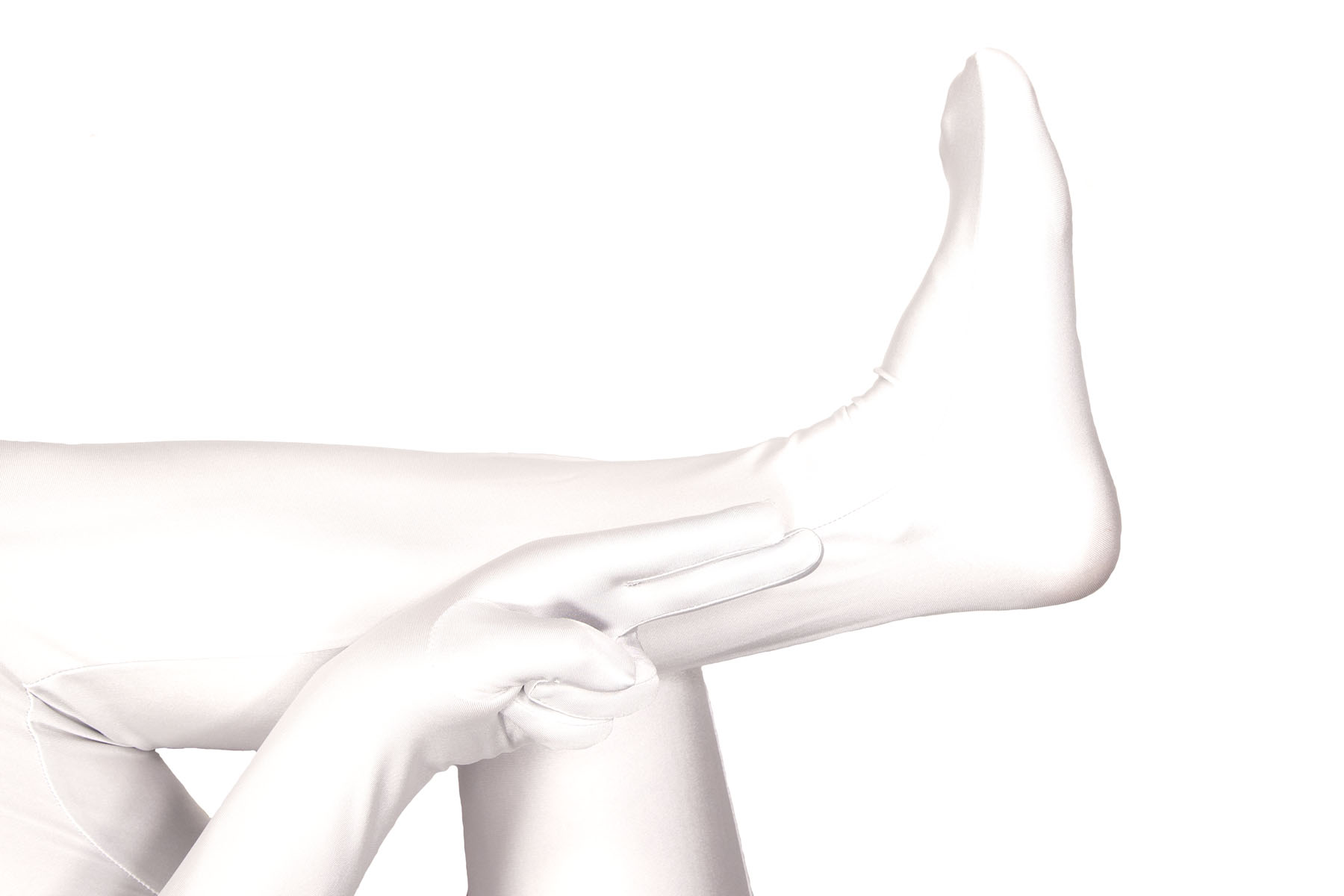 A seated person in a white bodysuit has crossed their left ankle over their right knee. Their left hand lies on top of the ankle, palm up. The index and middle fingers are extended, and the ring and pinkie fingers are folded.