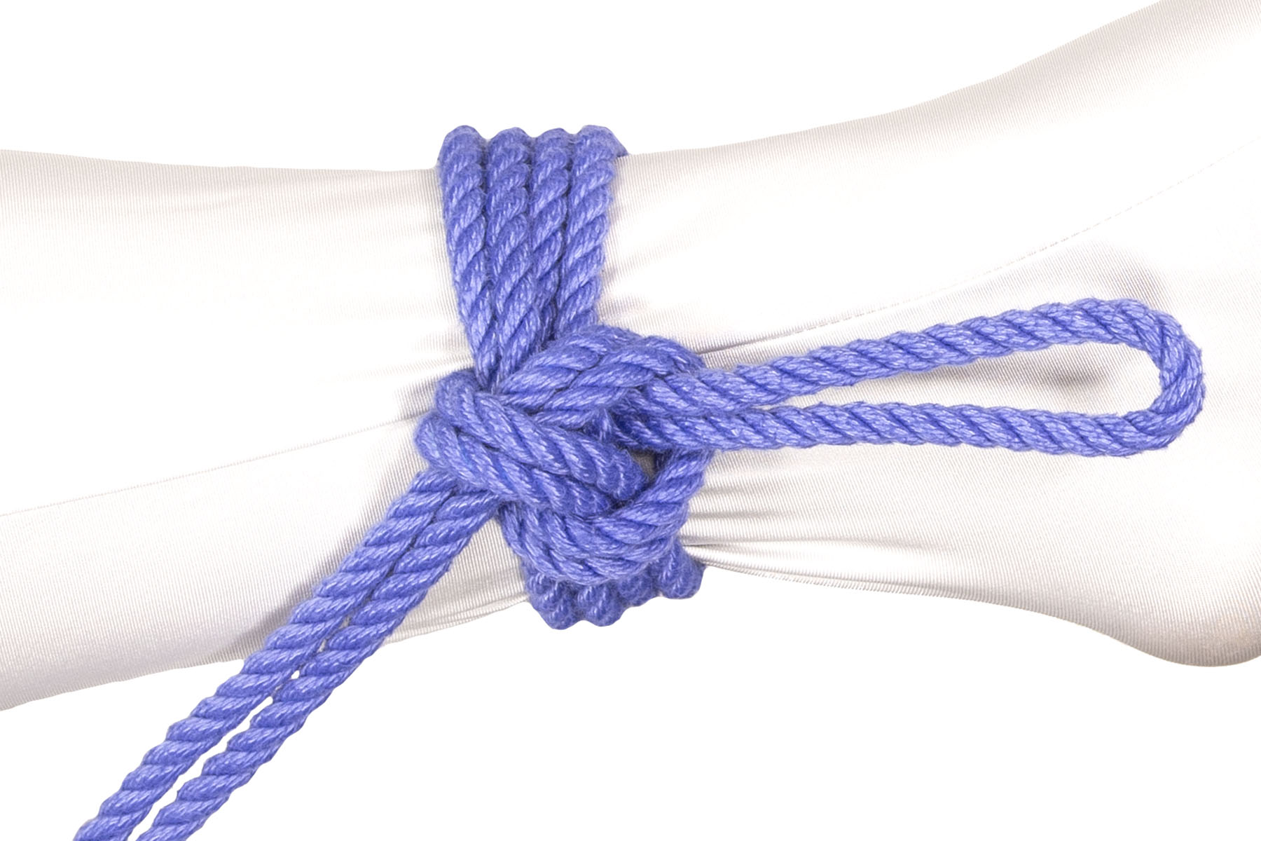 A Somerville bowline has been tied in doubled blue rope around the ankle of a person wearing a white bodysuit. The standing part of the rope enters from the lower left and joins the knot right above the ankle bone. Two double wraps circle the ankle and a three inch bight extends toward the heel.