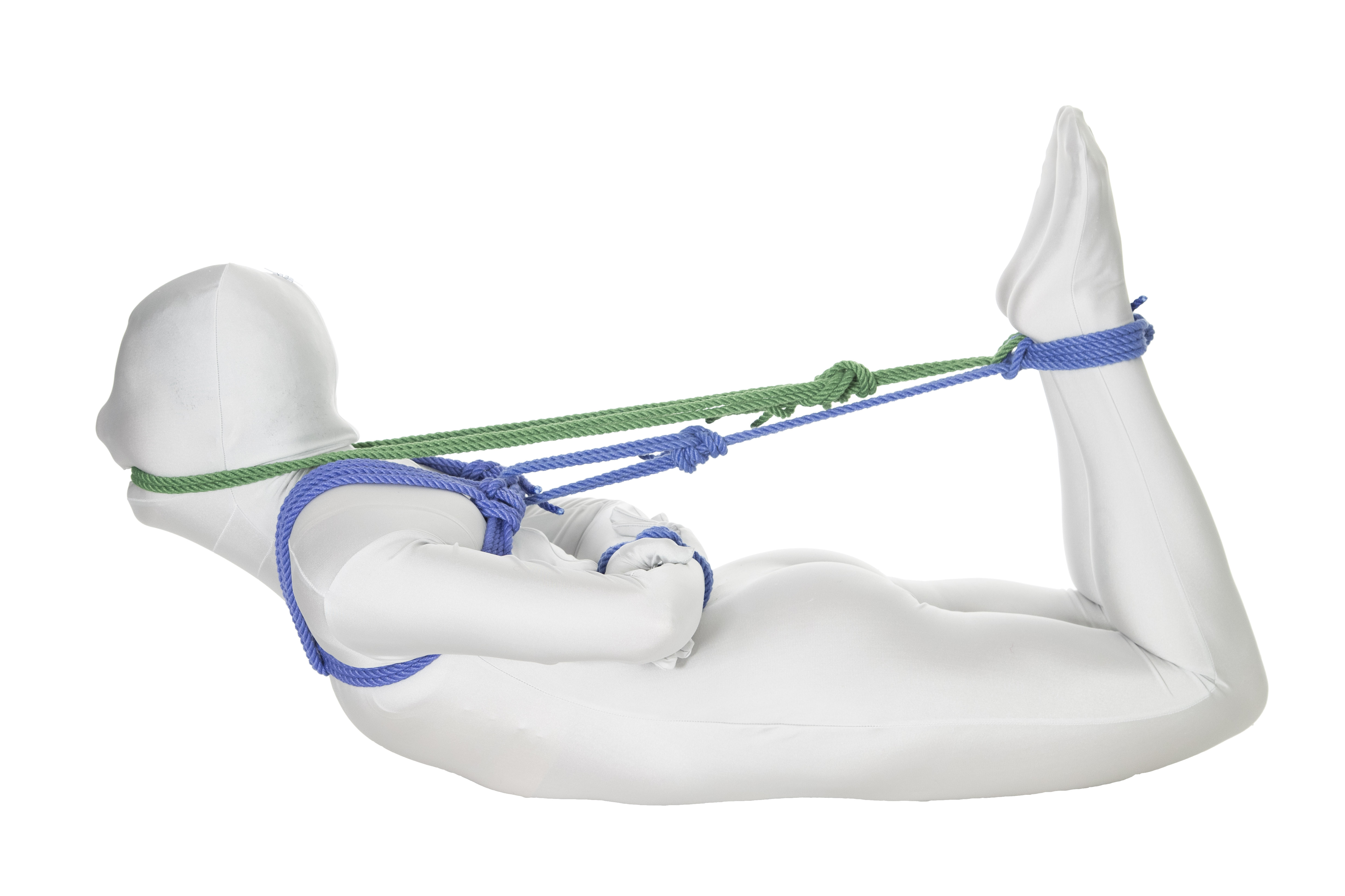 A person in a white bodysuit lying facedown in a hogtie position, with their hands tied behind their back and attached to their ankles with blue rope. They are gagged with a green rope tied to their ankles.