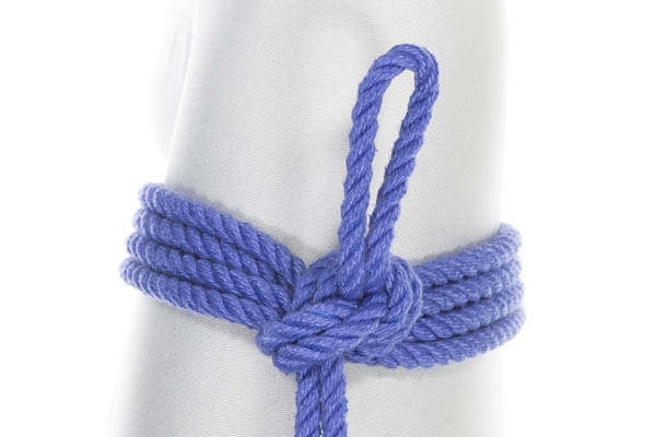 A Somerville Bowline tied in blue rope around the thigh of a person in a white bodysuit, just above the knee. Two double wraps of rope go around the thigh. The tail of the rope enters the frame from the bottom and enters a knot that lies on top of the wraps. A three inch bight of rope exits the knot and lies on top of the thigh, pointing toward the knee.