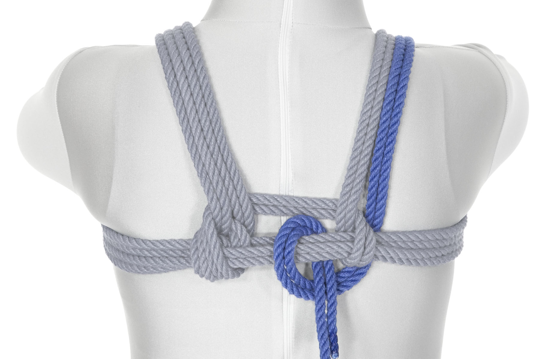 This is a rear view of the rope coming down from the shoulder on the outside of the first pass over the shoulder. It goes under the chest wraps, travels to the left, then comes over the chest wraps in between the left and right parts of the harness. It crosses back under the chest wraps just to the right, and over itself, making a half hitch.