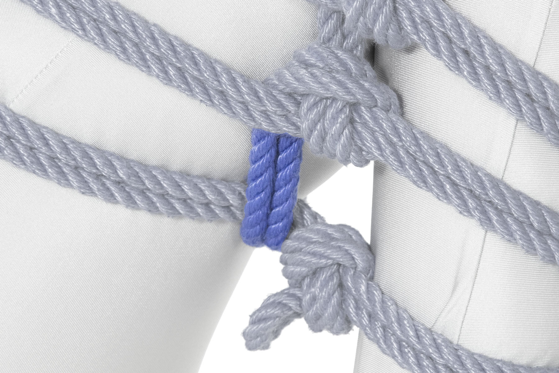 The rope crosses over the lowest wrap, right next to the single column tie. It turns inward and goes between the thigh and calf.